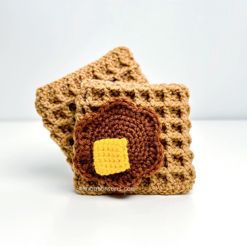 Pode incluir: Dois tapetes de waffle de croch&ecirc; com uma panqueca de croch&ecirc; marrom com um peda&ccedil;o de manteiga de croch&ecirc; amarelo no topo. Os tapetes s&atilde;o bege e a panqueca &eacute; marrom com um centro amarelo.