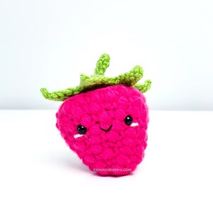 Peut inclure: Une fraise en crochet rose avec une tige et des feuilles en crochet vert. La fraise a un visage souriant avec des yeux noirs.