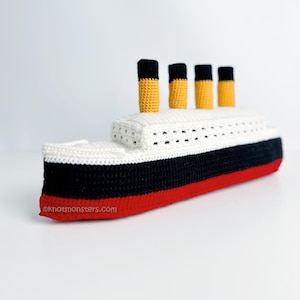 May include: A crocheted model of the Titanic, featuring a red hull, black midsection, and white upper deck. It has four yellow and black funnels. The website address oknotmonsters.com is visible on the hull. The model is made with yarn.