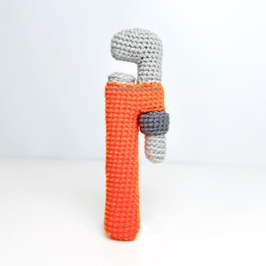 Könnte beinhalten: Ein gehäkelter Spielzeugschlüssel mit orangefarbenem Griff und grauen Metallteilen.