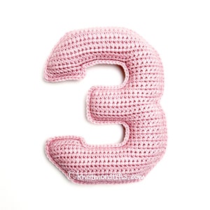 May include: A pink crocheted number three. The number is made with a single crochet stitch and is a soft, plush toy.