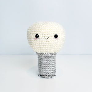 May include: A white crocheted lightbulb with a gray crocheted base and a smiling face with black eyes.