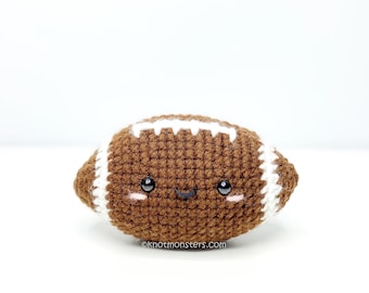 May include: A brown and white crocheted football with a smiling face. The football has black eyes and a stitched white line down the center.
