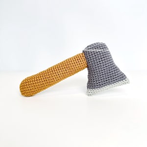 May include: A crocheted axe toy with a gray axe head and a yellow handle.