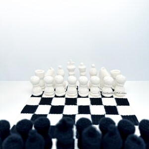 May include: A crocheted chess set with black and white pieces arranged on a checkered board. The white pieces are in focus, while the black pieces are blurred in the foreground. The board is black and white.