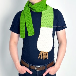 May include: A green and white crocheted scarf shaped like a leek. The scarf has a brown tassel at the bottom.