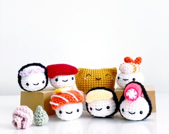 Op de afbeelding: Een set van zeven gehaakte sushi-knuffels, elk met een andere vulling en topping. De sushi zijn gerangschikt op een houten oppervlak.
