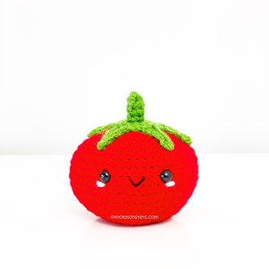 May include: A red crocheted tomato with a green crocheted stem and leaves. The tomato has a smiling face with black eyes.
