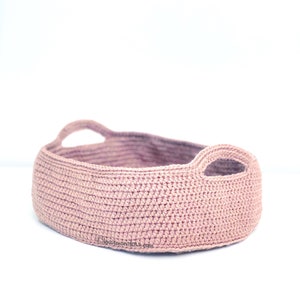 May include: A pink crocheted basket with two handles. The basket is oval shaped and has a textured surface.