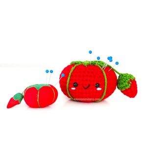 May include: Two crocheted tomato pincushions, one with a smiling face and pins sticking out, the other with a green leaf. Both are red with green leaves.