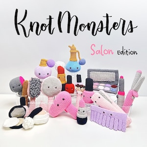 以下が含まれることがあります： ヘアドライヤー、口紅、マニキュア、香水瓶、メイクパレット、櫛、ブラシなど、かぎ針編みのサロンアイテムのコレクション。各アイテムには小さな黒い目と笑顔の口が付いています。テキストは「Knot Monsters Salon Edition」と書かれています。