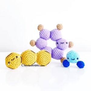 May include: Three crocheted amigurumi toys: a purple ring with brown accents, a yellow chain, and a blue figure with blue legs. Each toy has a smiling face.