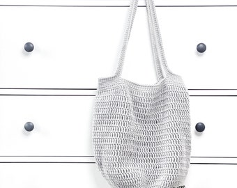 Peut inclure: Un sac cabas en crochet gris suspendu à une commode blanche avec des boutons noirs. Le sac a un fond large et plat et deux longues anses.