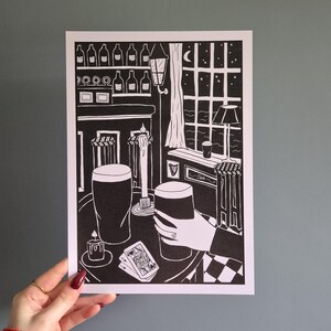 May include: Black and white illustration of a pub scene with two pints of beer, a lit candle, and playing cards on a checkered table. The scene is set at night with a window view of a moon and stars.