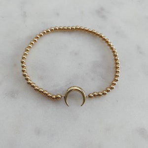 May include: A gold beaded bracelet with a crescent moon charm.