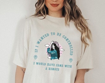 Pode incluir: Camiseta branca com um gráfico azul de uma mulher usando um chapéu e o texto "Se eu quisesse ser controlada, teria vindo com um controle remoto".