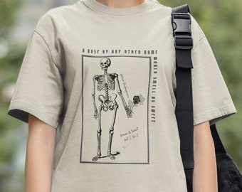 Puede incluir: Una camiseta beige con una ilustración en blanco y negro de un esqueleto sosteniendo una rosa. El texto "A rose by any other name would smell as sweet" está impreso en la camiseta.