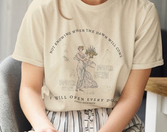 May include: A beige t-shirt with a vintage illustration of a woman holding flowers. The text "Not knowing when the dawn will come I will open every door Emily Dickinson" is printed on the shirt.