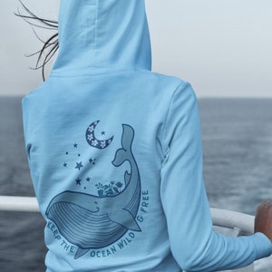 May include: Light blue hoodie with a whale graphic on the back. The whale is surrounded by stars and a crescent moon with flowers. The text "Keep the Ocean Wild & Free" is printed around the whale.