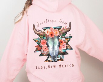 Può includere: Felpa rosa con un design di teschio floreale e il testo "Greetings from Taos, New Mexico".