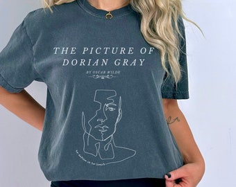 May include: A dark gray t-shirt with the text "The Picture of Dorian Gray by Oscar Wilde" and a line drawing of a face. The text "To define is to limit" is also included on the shirt.