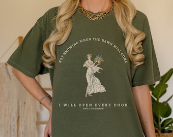 May include: A green t-shirt with a vintage illustration of a woman holding flowers. The text on the shirt reads "Not knowing when the dawn will come I will open every door Emily Dickinson".