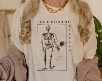 Puede incluir: Camiseta color crema con una ilustración en blanco y negro de un esqueleto sosteniendo una rosa. El texto "A ROSE BY ANY OTHER NAME WOULD SMELL AS SWEET" y "Romeo & Juliet Act 2. S. 2" están impresos en la camiseta.