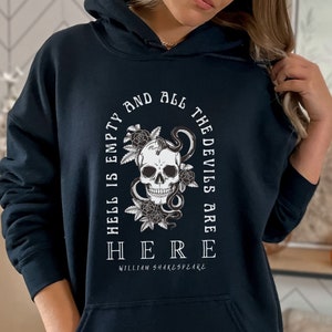 Op de afbeelding: Zwarte hoodie met een witte grafische print van een schedel met een slang eromheen. De grafiek bevat ook bloemen en de tekst "De hel is leeg en alle duivels zijn HIER William Shakespeare".
