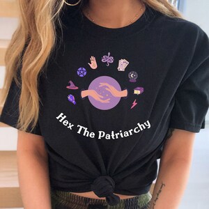 May include: Black t-shirt with a graphic of hands holding a purple orb surrounded by various witchy symbols. The text "Hex The Patriarchy" is printed below the graphic.