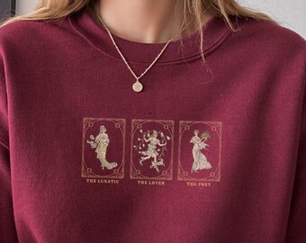 Op de afbeelding: Bordeauxkleurige trui met een afbeelding van drie tarotkaarten: De Dwaas, De Geliefde en De Priester. De kaarten zijn in gouden frames met een gouden achtergrond.