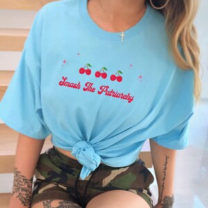 May include: A light blue t-shirt with a graphic of four red cherries and the text "Smash The Patriarchy" in pink lettering.