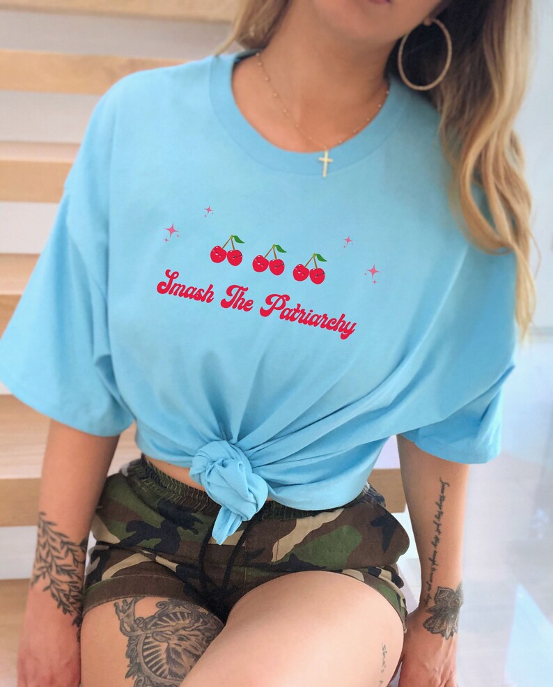 May include: A light blue t-shirt with a graphic of four red cherries and the text "Smash The Patriarchy" in pink lettering.