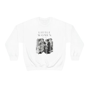 K&ouml;nnte beinhalten: Wei&szlig;er Pullover mit einem schwarzen grafischen Druck des Textes "LITTLE WOMEN" und einem Schwarzwei&szlig;bild von vier Frauen. Der Text "EST. 1868" ist unter dem Text "LITTLE WOMEN" gedruckt.