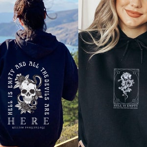 Puede incluir: Sudadera negra con un estampado gráfico blanco de una calavera con una serpiente enroscada alrededor y rosas. El texto "El infierno está vacío y todos los demonios están aquí" está impreso debajo del gráfico. El texto "William Shakespeare" está impreso debajo de la cita.