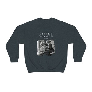 K&ouml;nnte beinhalten: Ein dunkelblauer Pullover mit einem grafischen Druck eines Schwarzwei&szlig;bildes von vier Frauen. Der Text "LITTLE WOMEN EST. 1868" ist in Wei&szlig; &uuml;ber dem Bild gedruckt.