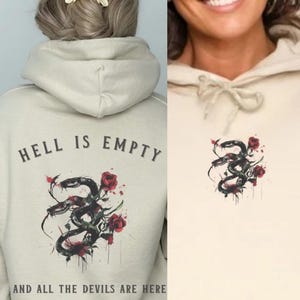 Puede incluir: Una sudadera con capucha beige con el texto "Hell is empty and all the devils are here" impreso en la espalda. La parte delantera de la sudadera con capucha presenta una serpiente negra con rosas rojas.