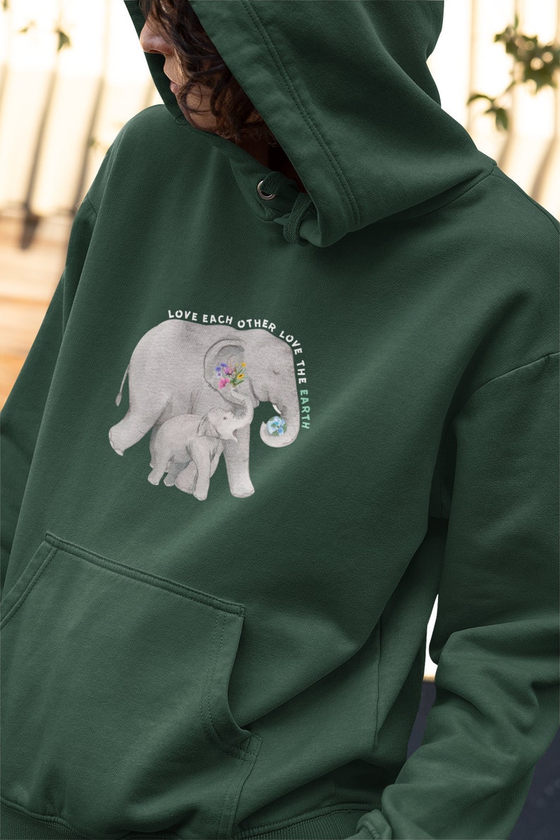 Op de afbeelding: Groen hoodie met een afbeelding van twee olifanten, waarvan er &eacute;&eacute;n een wereldbol vasthoudt. De tekst "Love Each Other Love The Earth" is in een cirkel rond de olifanten gedrukt.