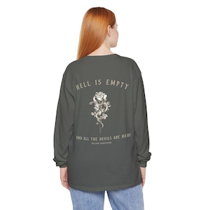Puede incluir: Una camiseta de manga larga verde oscuro con un gráfico de una rosa blanca y una serpiente en la espalda. El texto "Hell is empty and all the devils are here" está impreso debajo del gráfico, con "William Shakespeare" en una fuente más pequeña debajo del texto.