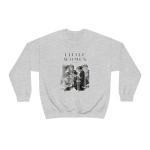 K&ouml;nnte beinhalten: Ein grauer Pullover mit einem schwarz-wei&szlig;en Grafikdruck einer Gruppe von Frauen. Der Text "LITTLE WOMEN" ist &uuml;ber dem Grafikdruck gedruckt, mit dem Text "EST. 1868" unter dem Grafikdruck.