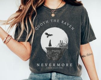 May include: Dark gray t-shirt featuring a graphic design inspired by Edgar Allan Poe's poem, "The Raven." The design includes a raven, a figure on a cliff, a full moon, and the words "Quoth the Raven" and "Nevermore."