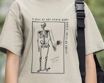 Puede incluir: Una camiseta beige con una ilustración en blanco y negro de un esqueleto sosteniendo una rosa. El texto "A rose by any other name would smell as sweet" está impreso en la camiseta. El texto "Romeo & Juliet Act 2. Sc. 2" también está impreso en la camiseta.
