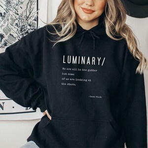 May include: Black hooded sweatshirt with a white print that reads "LUMINARY/ We are all in the gutter but some of us are looking at the stars. - Oscar Wilde"