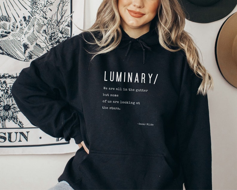 May include: Black hooded sweatshirt with a white print that reads "LUMINARY/ We are all in the gutter but some of us are looking at the stars. - Oscar Wilde"