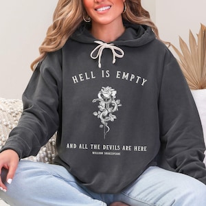 May include: A dark grey hoodie with a white graphic print of a rose with a snake wrapped around it. The text "Hell is empty and all the devils are here" is printed below the rose, with the attribution "William Shakespeare" underneath.