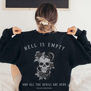 Puede incluir: Sudadera negra con un gráfico de calavera y serpiente y el texto "El infierno está vacío y todos los demonios están aquí" de William Shakespeare.