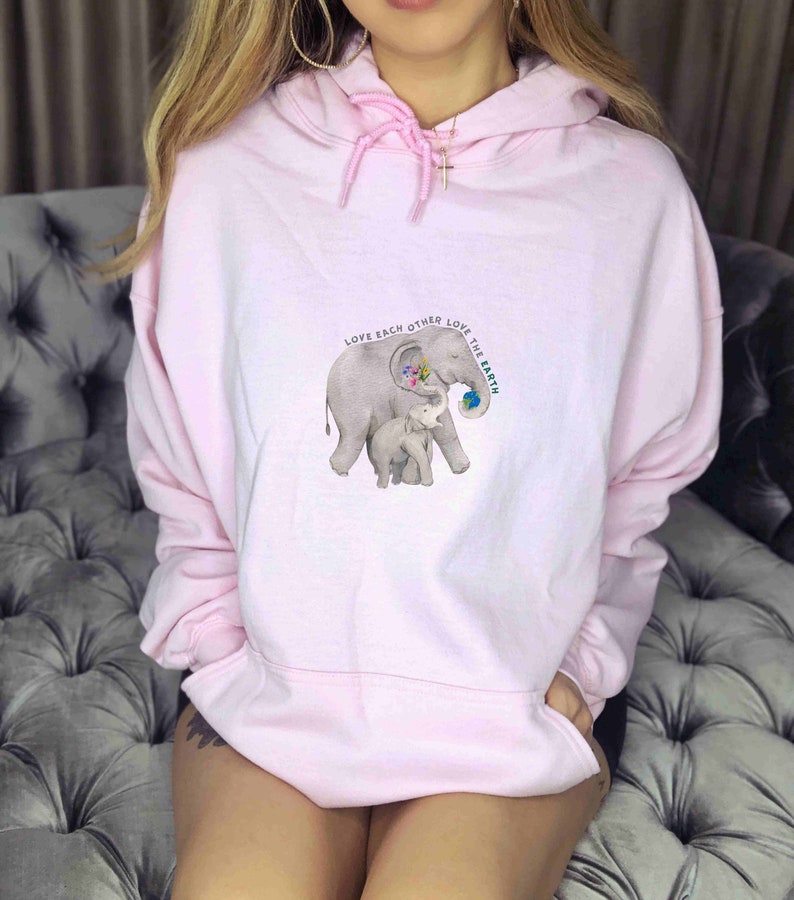 Op de afbeelding: Roze hoodie met een afbeelding van twee olifanten en de tekst "Love each other Love the Earth".