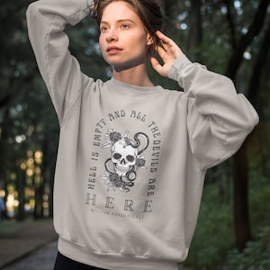 Könnte beinhalten: Ein hellgraues Sweatshirt mit einem Totenkopf- und Schlangenmotiv. Der Text auf dem Sweatshirt lautet "Die Hölle ist leer und alle Teufel sind hier" und "William Shakespeare".