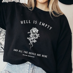 Puede incluir: Sudadera negra con un estampado gr&aacute;fico blanco de una rosa con una serpiente enroscada a su alrededor. El texto "El infierno est&aacute; vac&iacute;o y todos los demonios est&aacute;n aqu&iacute;" est&aacute; impreso debajo de la rosa, con la atribuci&oacute;n "William Shakespeare" debajo.