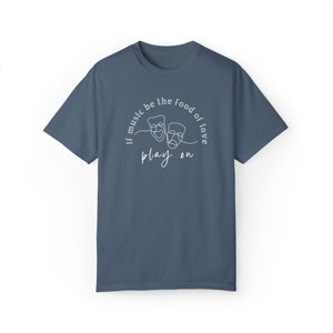 May include: A dark blue t-shirt with a white design featuring two theatre masks and the text "If music be the food of love play on".