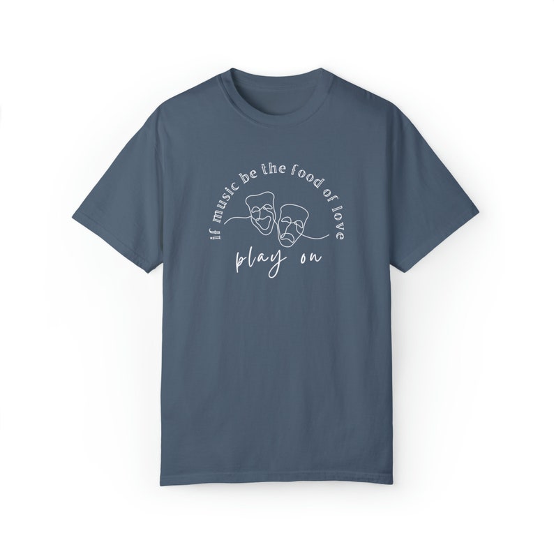 May include: A dark blue t-shirt with a white design featuring two theatre masks and the text "If music be the food of love play on".